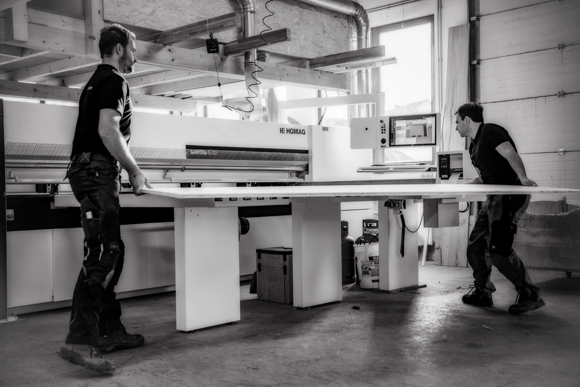 Zwei Schreiner legen ein Werkstück in eine HOMAG Verarbeitungsmaschine ein - Bild schwarz-weiß
